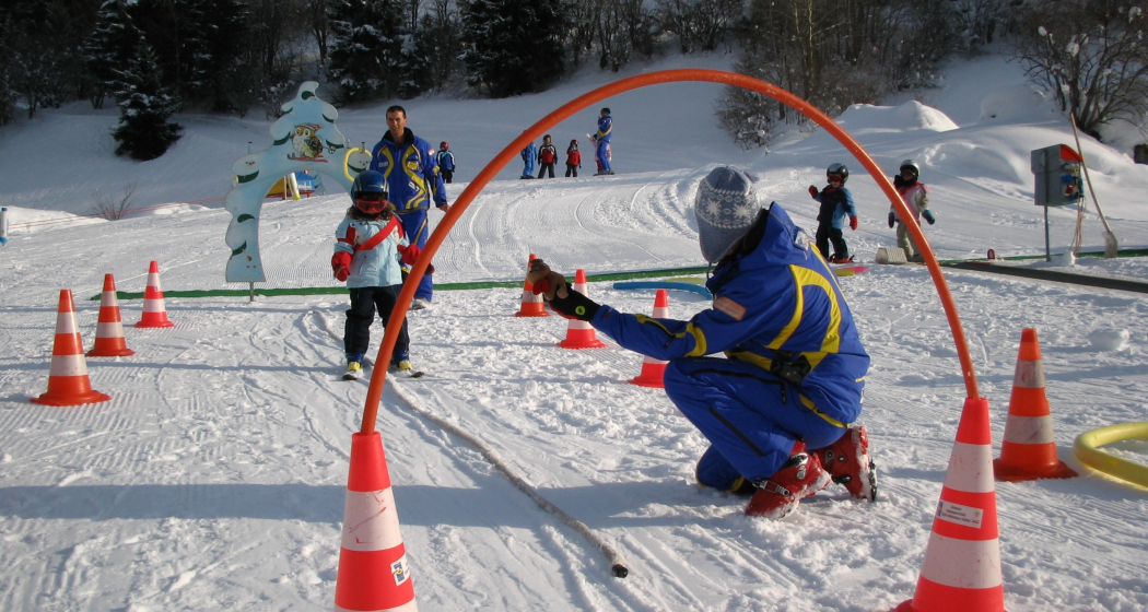 Das Foto zeigt einen Skilehrer der ein junges Mädchen das Skifahren beibringt