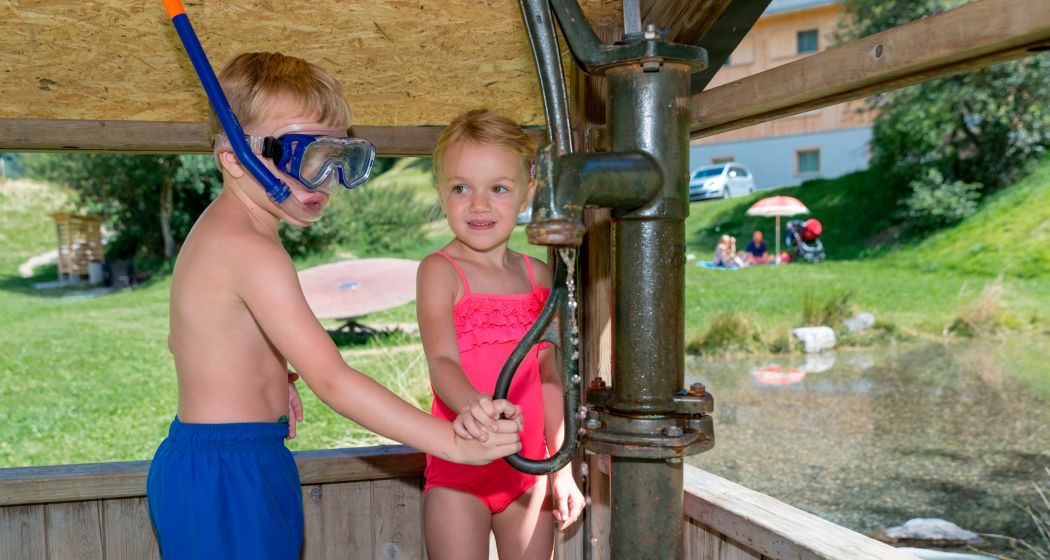 Das Foto zeigt zwei Kinder die mit einer Wasserpumpe spielen Das Foto zeigt zwei Kinder die mit einer Wasserpumpe spielen