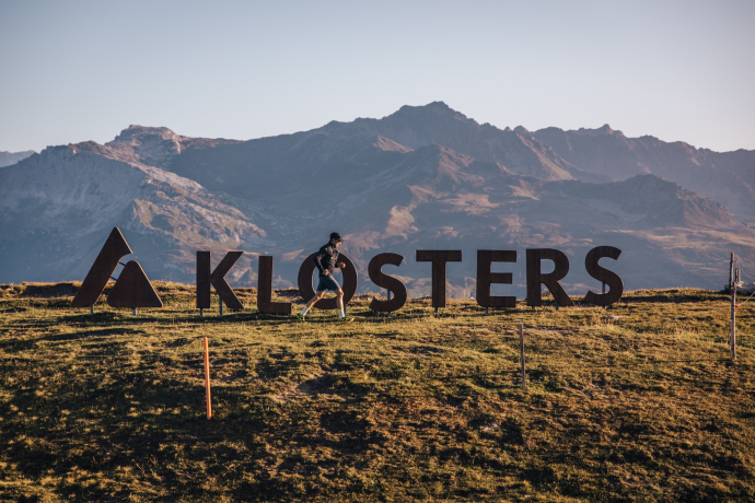 Ein Trailrunner läuft vor dem Klosters-Logo auf dem Gotschna Ein Trailrunner läuft vor dem Klosters-Logo auf dem Gotschna